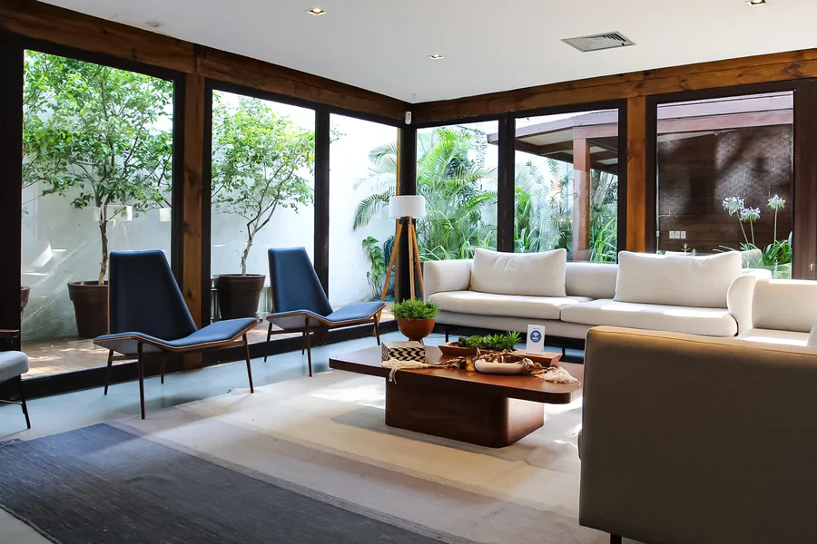 Sala de estar com sofás e poltronas, com janelas de vidro voltadas para o jardim